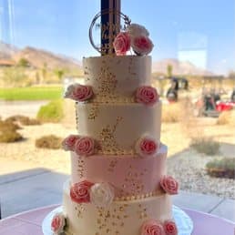 Tall pink tiered cake decorated with roses and gold accents